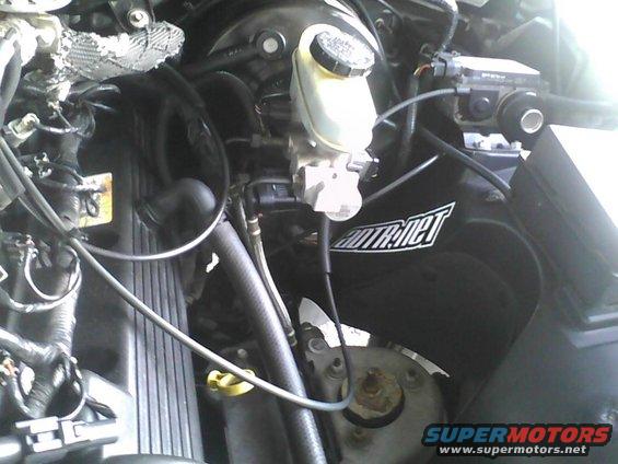 Engine bay showing brake fluid reservoir, hoses, and a black air intake cover with 'AUTOTR.NET' logo