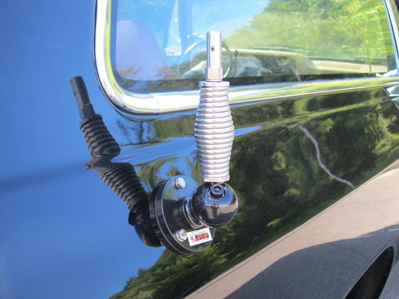 Black vehicle fender with chrome trim and a chrome antenna mount a coiled spring