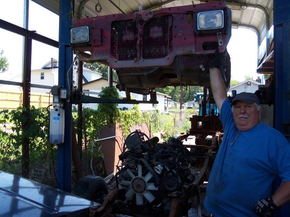 Man holds up red vehicle front end with engine below, outdoors