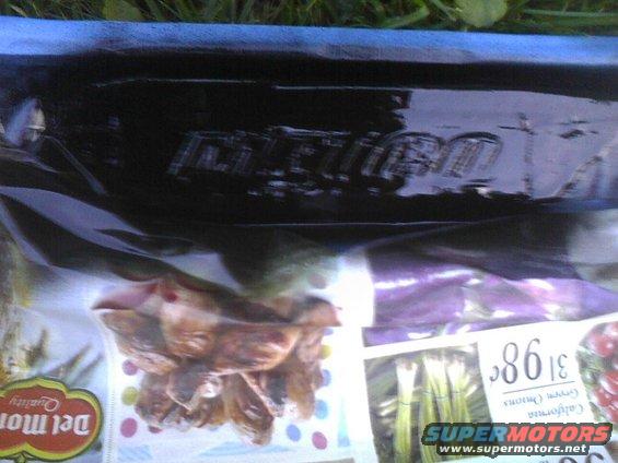 Black car part with embossed text, over a grocery bag and newspaper