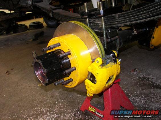 Yellow brake caliper and rotor assembly on a red jack stand