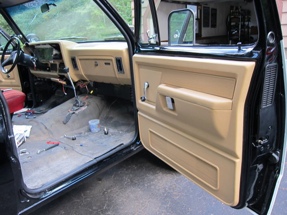 Interior of a truck with the driver's door open, showing the dashboard and floor with tools and parts scattered around