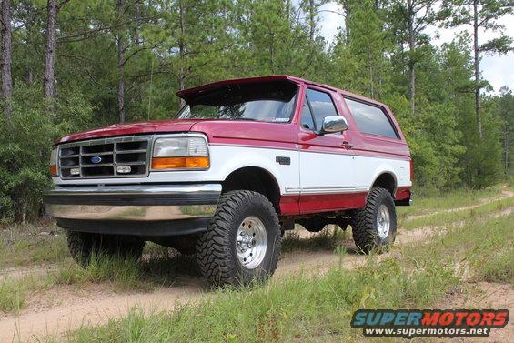 Red and white Ford Bronco on a dirt road with trees in the background
