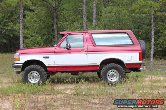 Red and white Ford Bronco parked in a grassy area with trees in the background