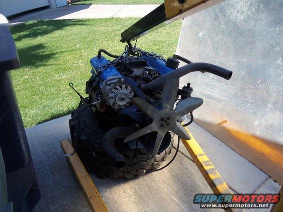 Blue engine with fan and alternator on a tire, supported by an engine hoist