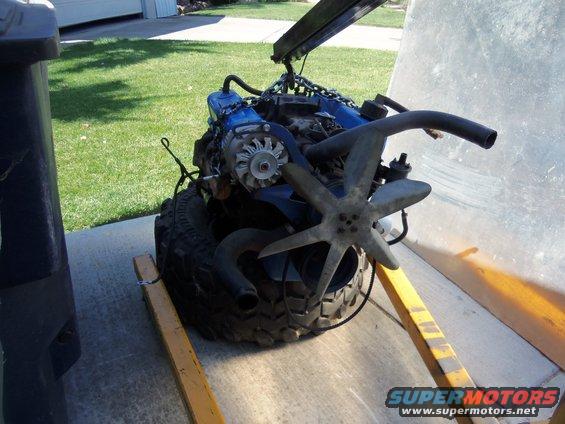 Blue engine with fan and alternator, resting on a tire and engine stand