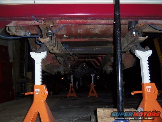 Undercarriage of a red vehicle on jack stands, showing suspension components
