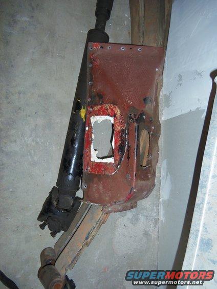 Rusty red metal panel with cutouts next to a black driveshaft