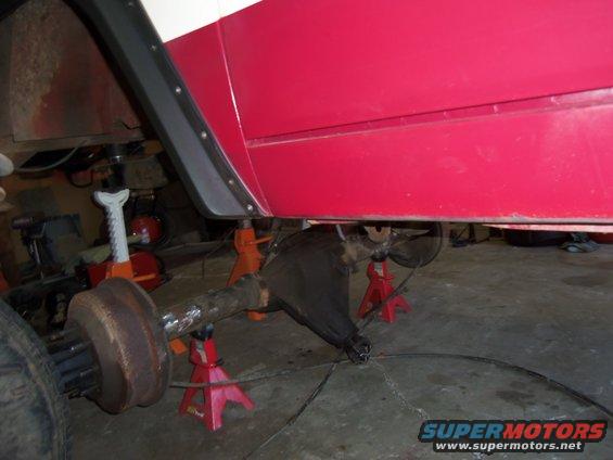 Rear axle assembly on red jack stands, part of a vehicle body in red and white visible above