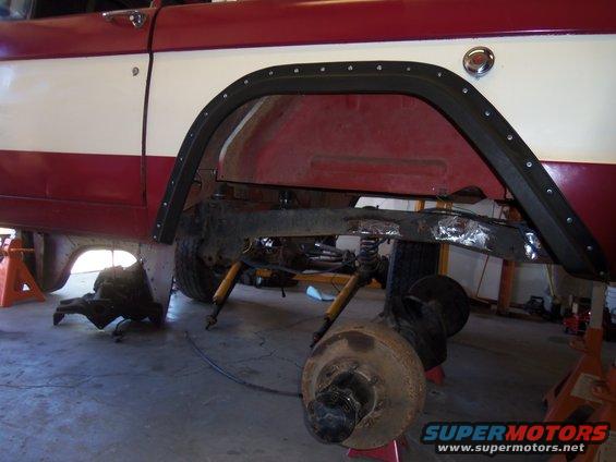 red and white vehicle on jack stands, rear axle removed, transmission visible underneath