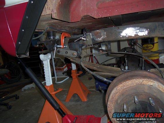 underbody of a vehicle on jack stands, showing suspension work with a C-clamp