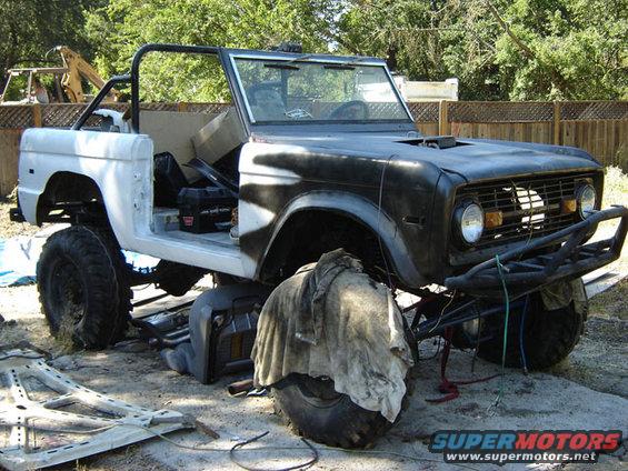 Ford Bronco body, partially painted, with roll cage and aftermarket bumper. It's on jack stands with parts around it