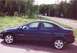 2000 Dodge Neon - A dark blue 2000 Dodge Neon sedan is parked on the side of a rural road with trees and a "S HOOL" sign in the background.