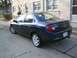 2000 Dodge Neon - A dark blue 2000 Dodge Neon sedan is parked on a cracked concrete driveway in front of a stone building.