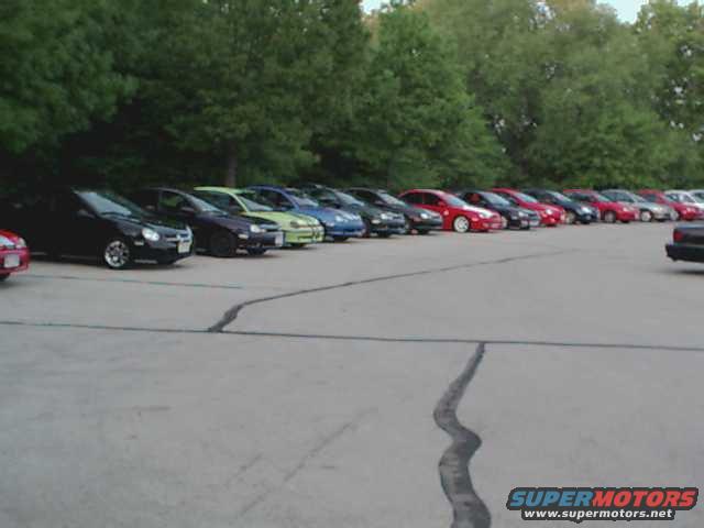 Line of sedans parked in a lot, with trees in the background. A watermark reads SUPERMOTORS