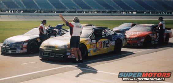 Race cars lined up on the track, one with a person waving. The car in front has 'TAURUS' on it and number 312