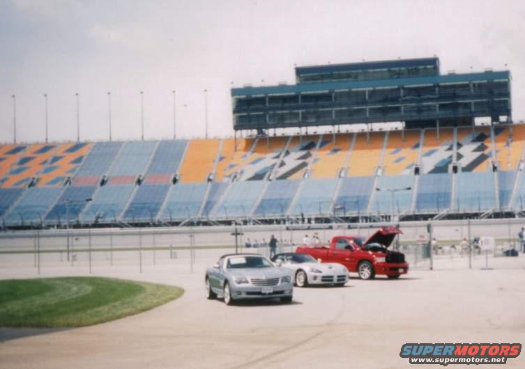 Silver convertible, white sports car, and red pickup truck parked in front of stadium seating