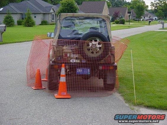 Brown Jeep Wrangler with spare tire on rear, surrounded by orange safety netting and cones