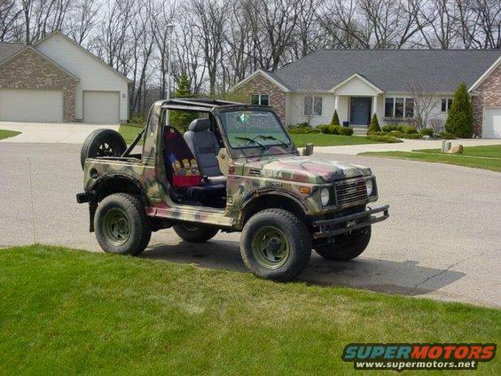 Suzuki Samurai with camouflage paint, spare tire on back, doors removed, parked on a suburban street