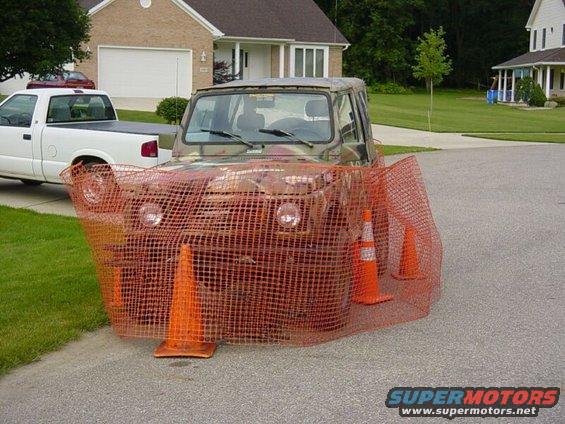 Camouflaged off-road vehicle behind orange safety netting and traffic cones