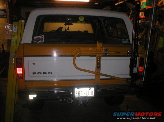 Yellow and white 1978 Ford Bronco rear view with a yellow swing-away spare tire carrier and a Hi-Lift jack mounted on the side