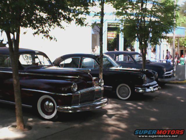 Three old sedans parked in a row, with trees casting shadows
