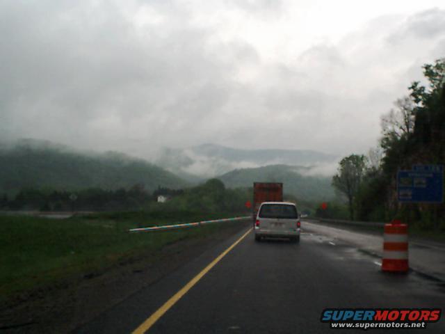Van driving on a wet highway with mountains in the background under a cloudy sky