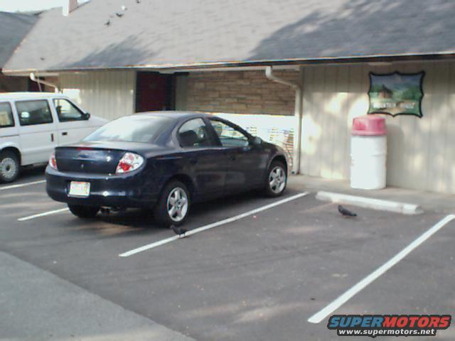 Dark blue sedan parked in a lot, rear view. White van to the left