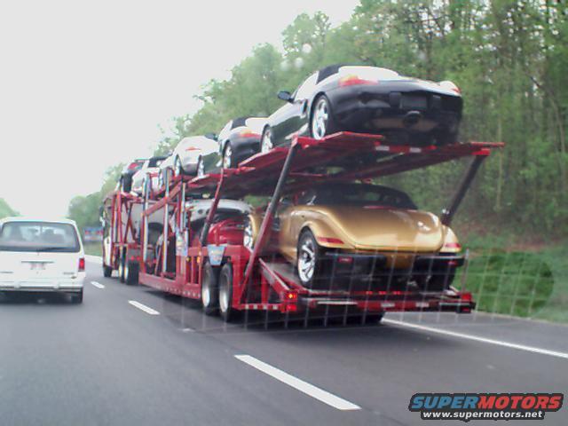 Car carrier truck with gold and black convertibles on a highway