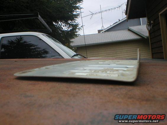 Rear of white vehicle with tinted windows, seen from low angle over rusty surface