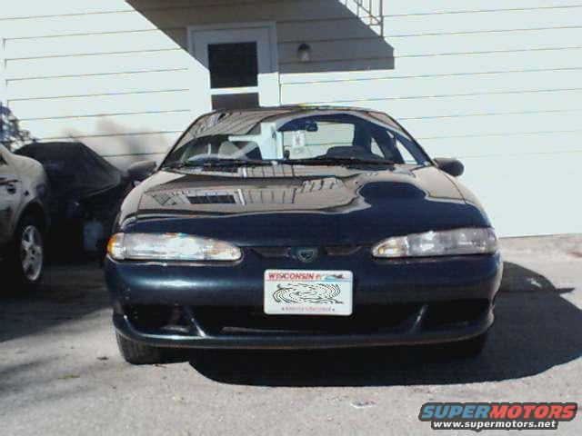 Dark blue sedan front view, parked in front of a building. License plate visible
