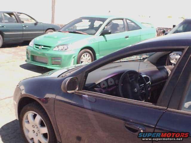Interior of dark sedan, dashboard and steering wheel visible. Green coupe in background