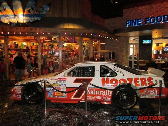 Side view of a white and orange Hooters #7 NASCAR race car with various sponsor decals