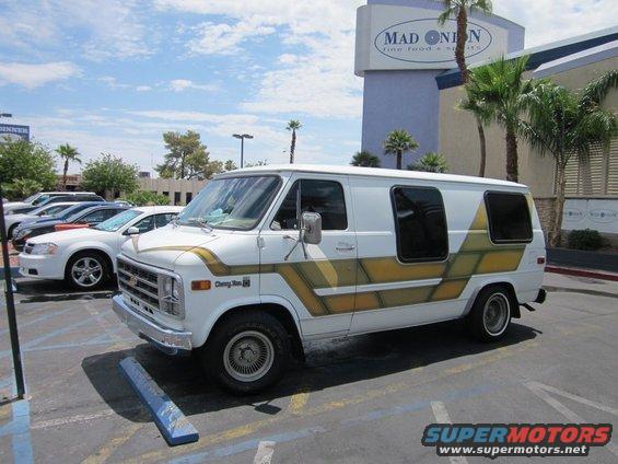 White Chevrolet van with gold stripes parked in a lot. Text on side says "Chevy Van."
