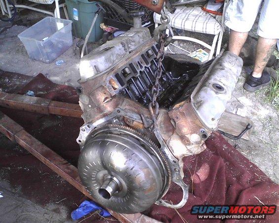 Engine and torque converter assembly suspended by chains, resting on a red cloth and wooden beams