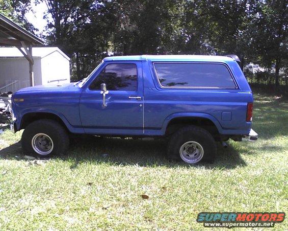 Blue Ford Bronco with aftermarket wheels parked on grass