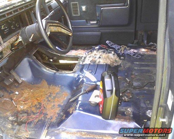 Interior of a 1985 Ford Bronco showing rusted floor, dashboard, and steering wheel