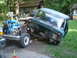 1979 Ford Bronco - A green truck cab and chassis, with a blue engine visible, sits in a yard with a wooden building in the background.