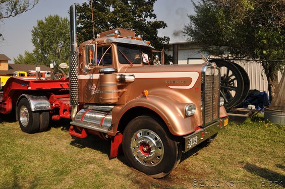 Copper Kenworth semi-truck with a red trailer, showing the Kenworth badge on the fender and a 1959 license plate