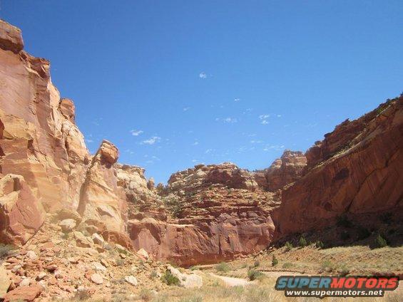 Desert canyon with red rock formations and a dirt road under a clear blue sky