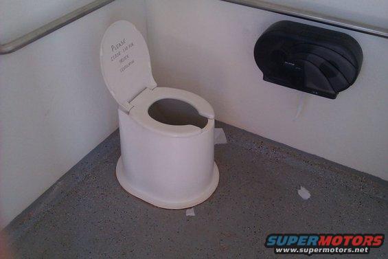 Portable toilet with handwritten note on lid: 'Please close lid for privacy. Thank you.'