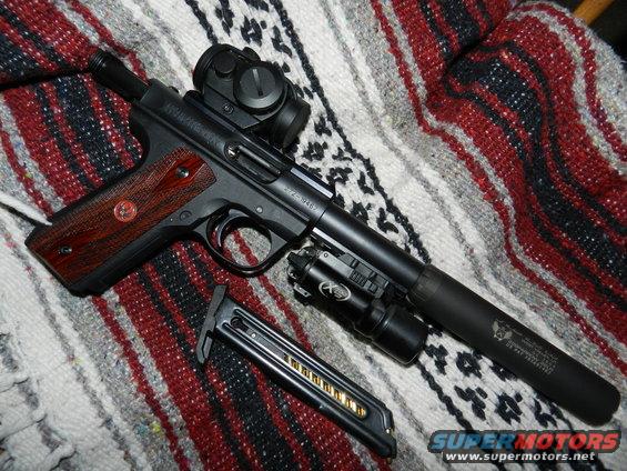 Pistol with red dot sight, suppressor, and flashlight, next to a loaded magazine. It's all on a striped blanket