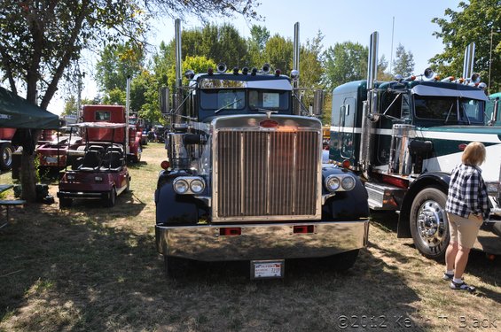 Black semi-truck with chrome grille and dual exhaust stacks, parked on grass
