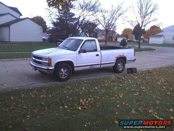 White pickup truck parked on a street with fallen leaves on the grass. It has a single cab and a long bed