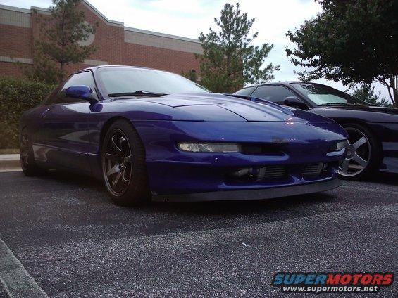 Blue sports coupe parked next to another car. Has aftermarket wheels and a front lip