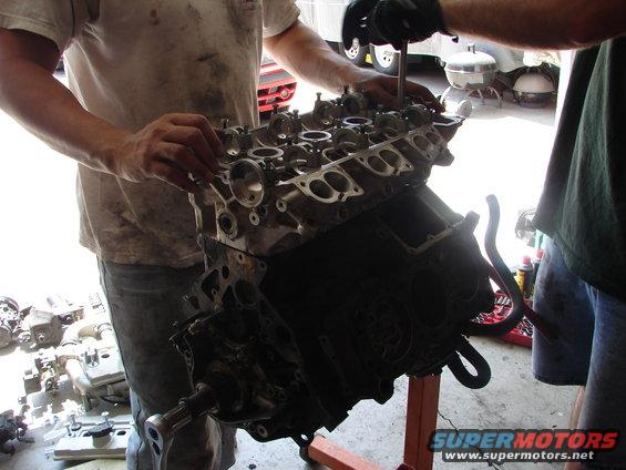 Engine block on stand, hands working on valve cover area