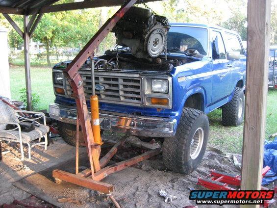 Blue Ford Bronco with engine hoist lifting out the engine. Lifted suspension and large tires