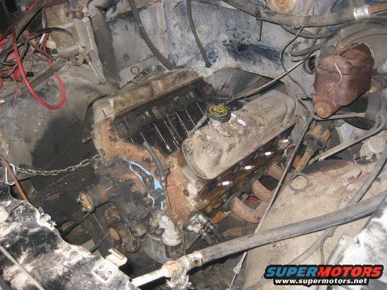 Engine bay with V8 engine, hoses, and wiring visible. Some parts appear rusty