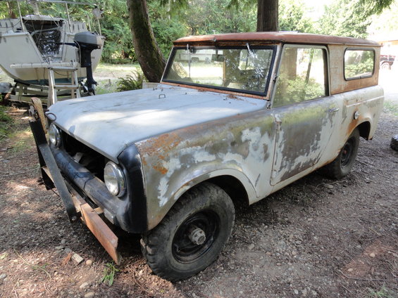 Rusty old SUV with a hardtop, parked on gravel. Boat on trailer in background
