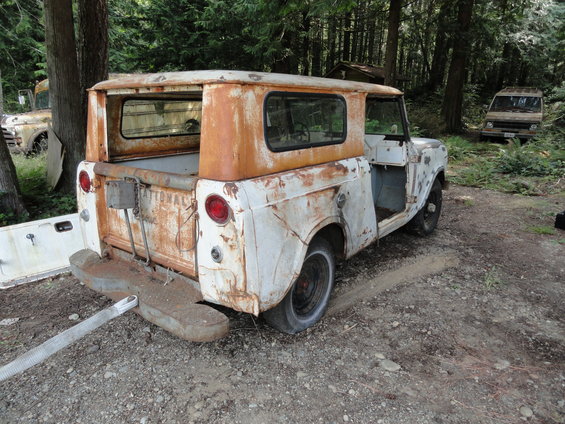 Rusted 1962 International Scout 80 with doors removed, parked in a wooded area. Another vehicle is visible in the background